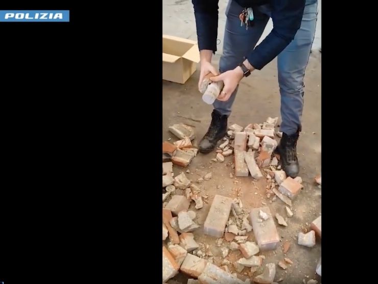 Un poliziotto rompe con le mani un mattoncino di cemento contenente eroina