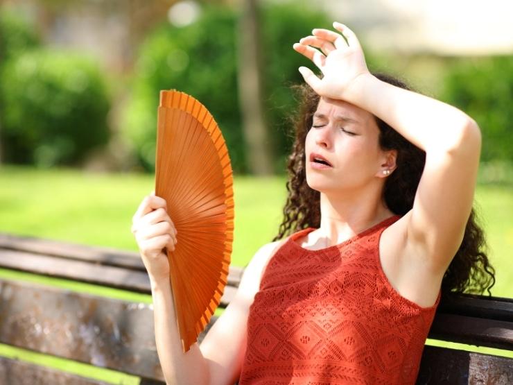 Una ragazza seduta al parco al sole tenta di rinfrescarsi con un ventaglio