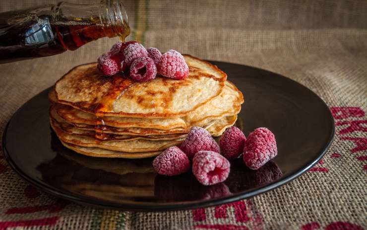 pancakese sopra un piatto con dei mirtilli e dello sciroppo di acero