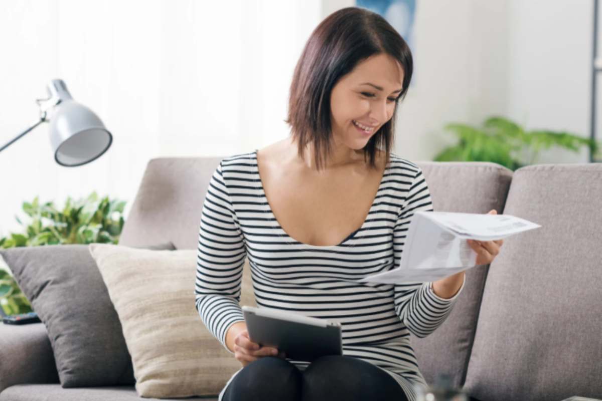 donna che sorride mentre legge dei fogli con in mano un tablet