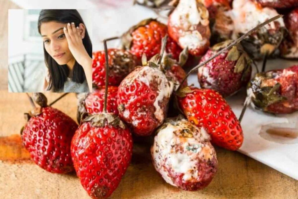 fragole con la muffa e donna con una mano su una tempia
