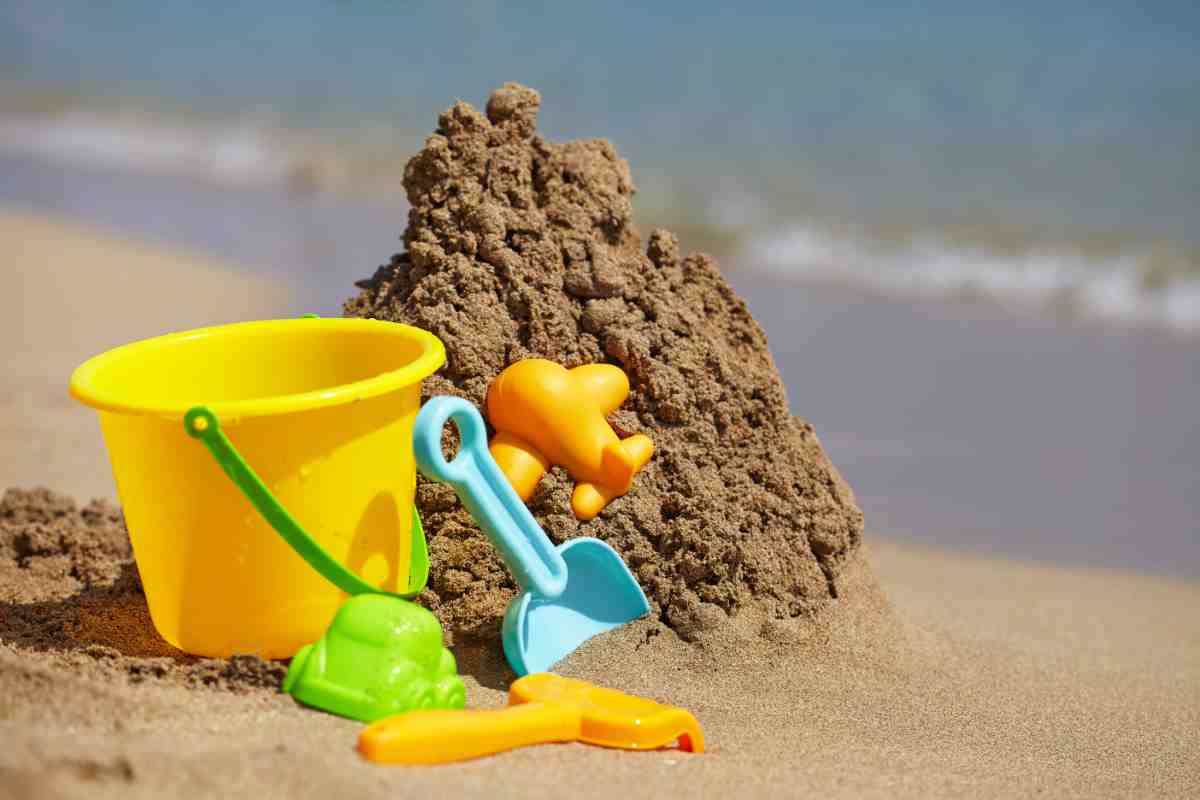 secchiello e palette in plastica vicino a un cumulo di sabbia bagnata su una delle spiagge per famiglie con bambini