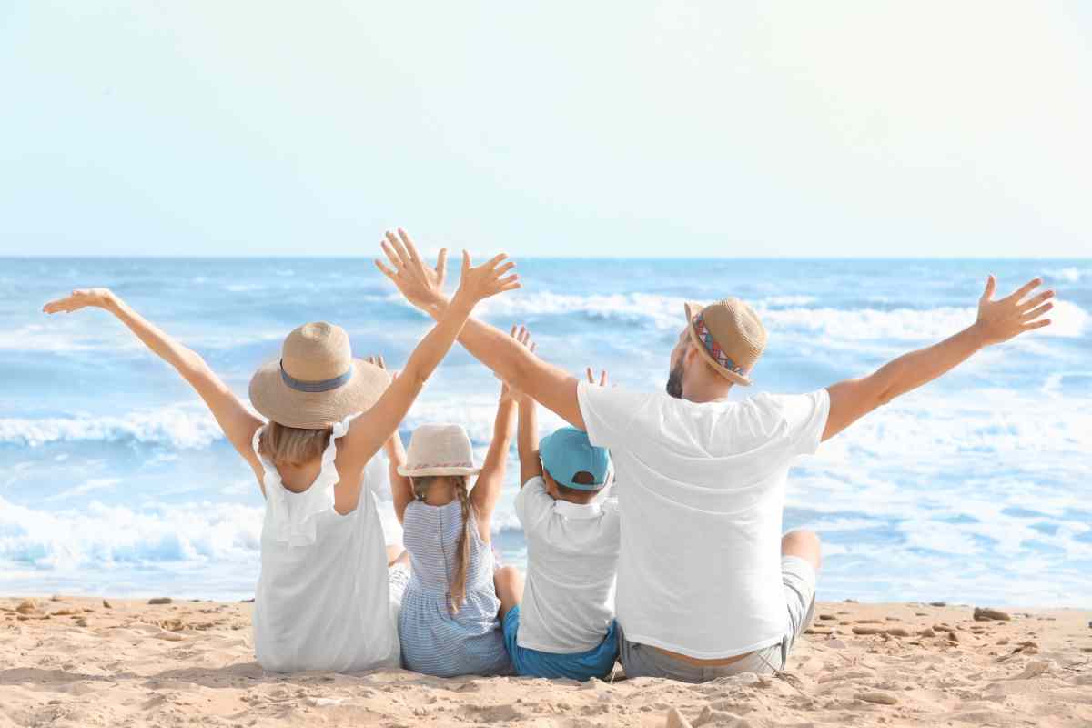famiglia con due bambini piccoli con le braccia alzate seduti su una spiaggia in riva al mare