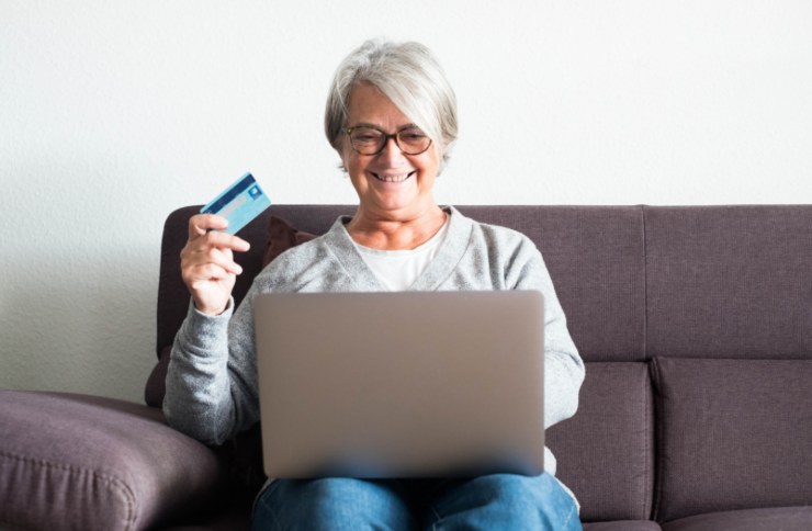 donna seduta sul divano con il computer sulle ginocchia e il bancomat in mano