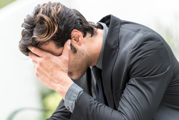 uomo disperato che si copre la faccia con una mano