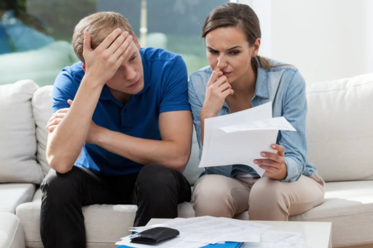 uomo e donna seduti sul divano che leggono dei fogli con espressione preoccupata