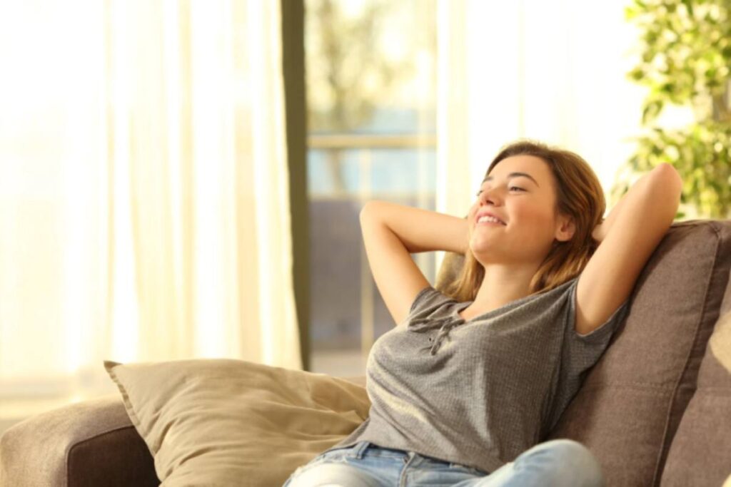 ragazza che sorride seduta sul divano con le mani dietro alla testa