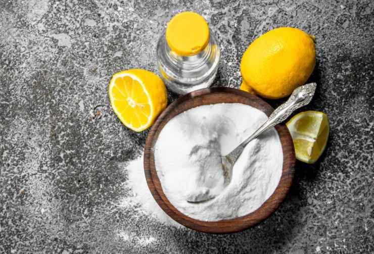 ciotola con dentro bicarbonato di sodio e accanto dei limoni e un bottiglino con dentro aceto