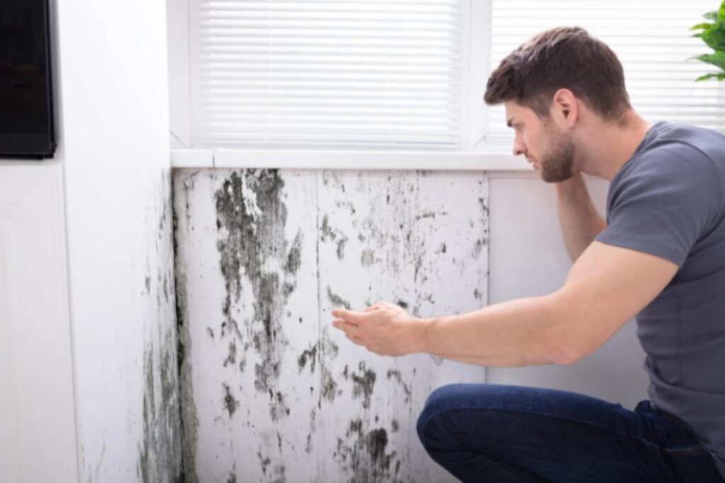 uomo che guarda la muffa sulle piastrelle del bagno