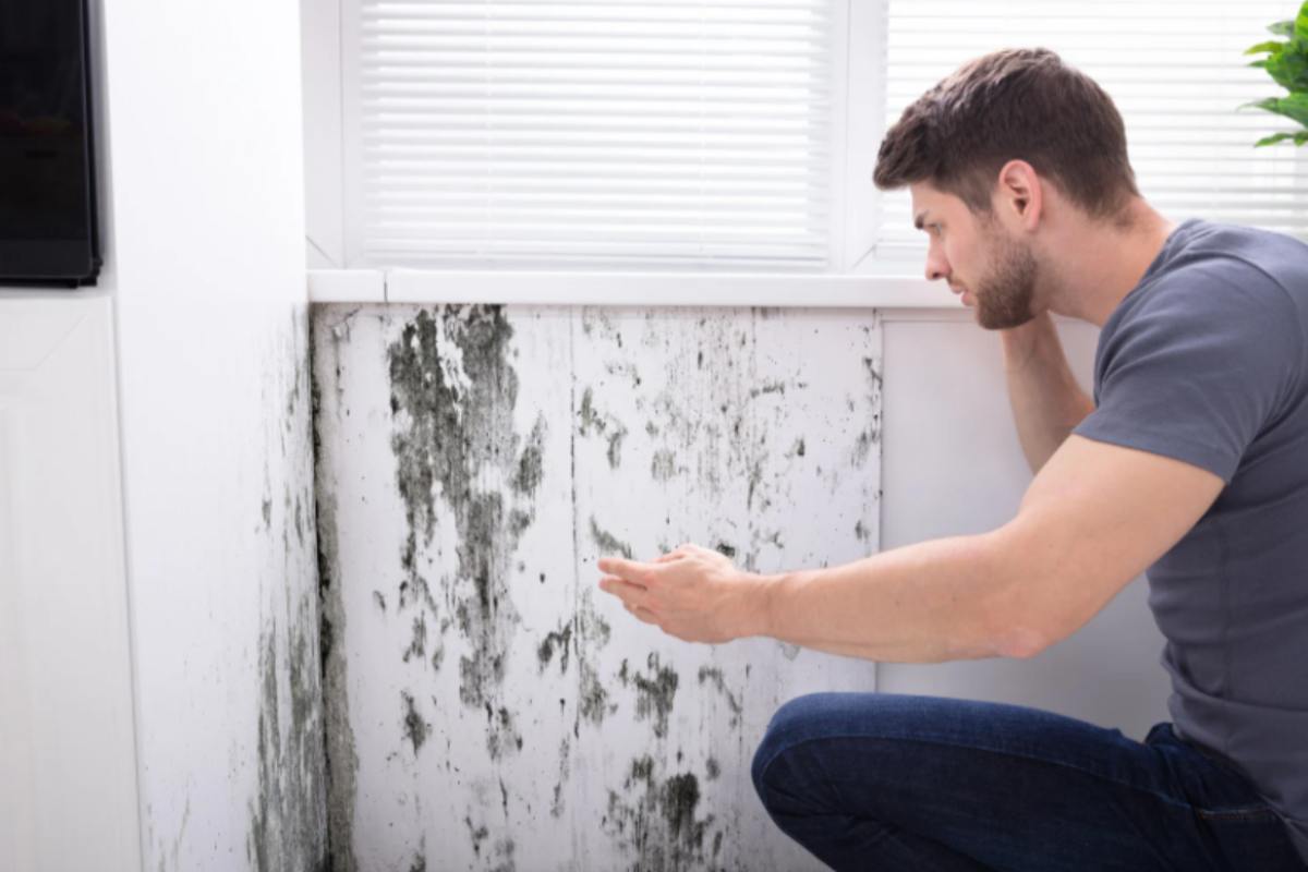 uomo che guarda la muffa sulle piastrelle del bagno