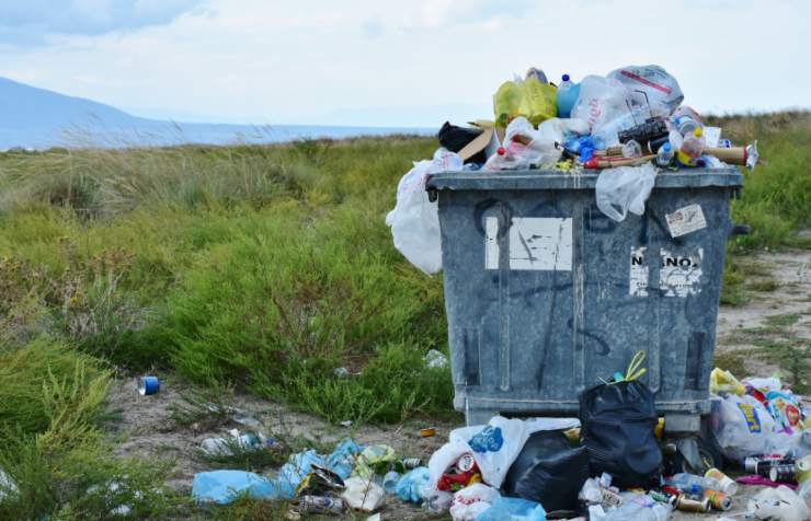 bidone pieno di rifiuti in mezzo ad un prato