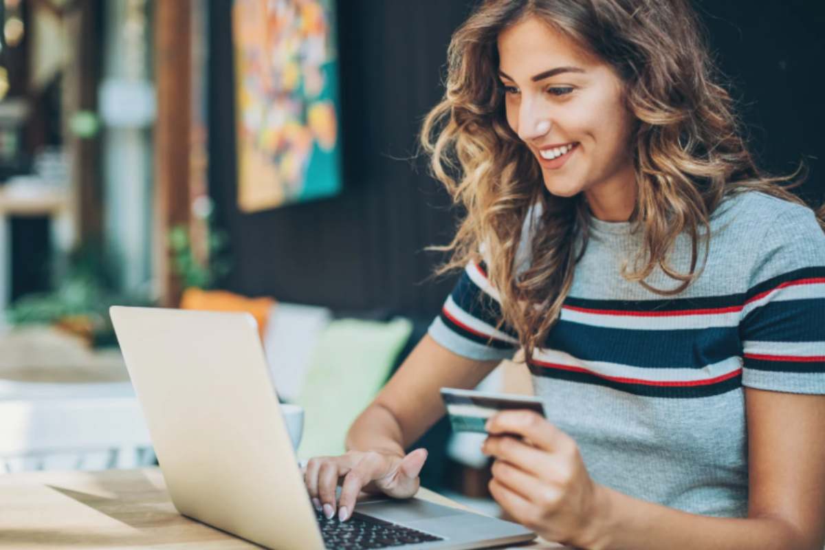 ragazza sorridente con un bancomat in mano seduta di fronte al computer