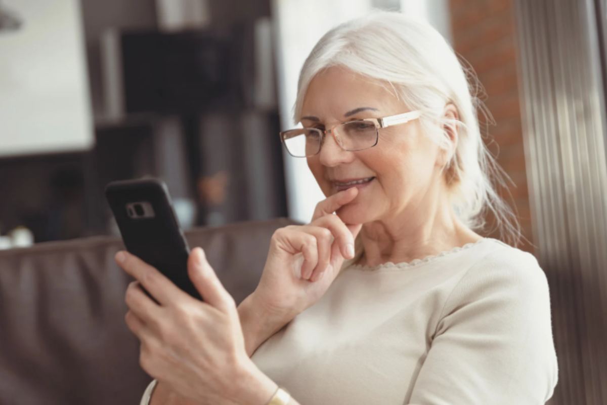 donna anziana seduta che guarda il cellulare e sorride