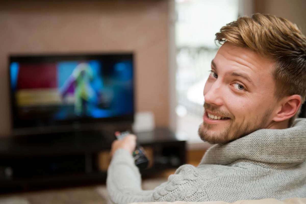 Uomo che sorride con telecomando verso TV accesa