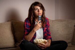 Donna seduta sul divano con telecomando e popcorn