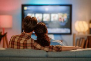 Un uomo e una donna seduti di spalle sul divano che guardano la TV