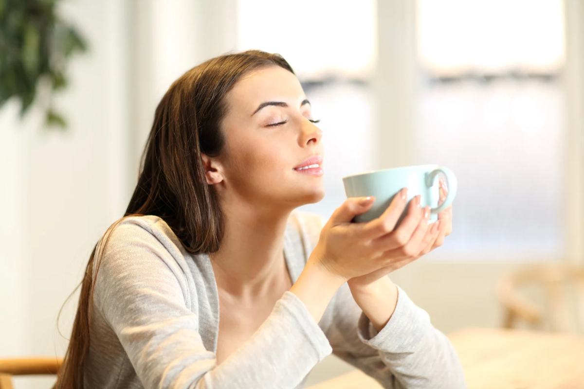 Donna che sorride con tazza in mano e occhi chiusi