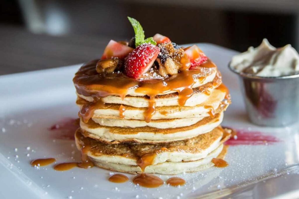 Pila di pancake in un piatto con frutta fresca e sciroppo