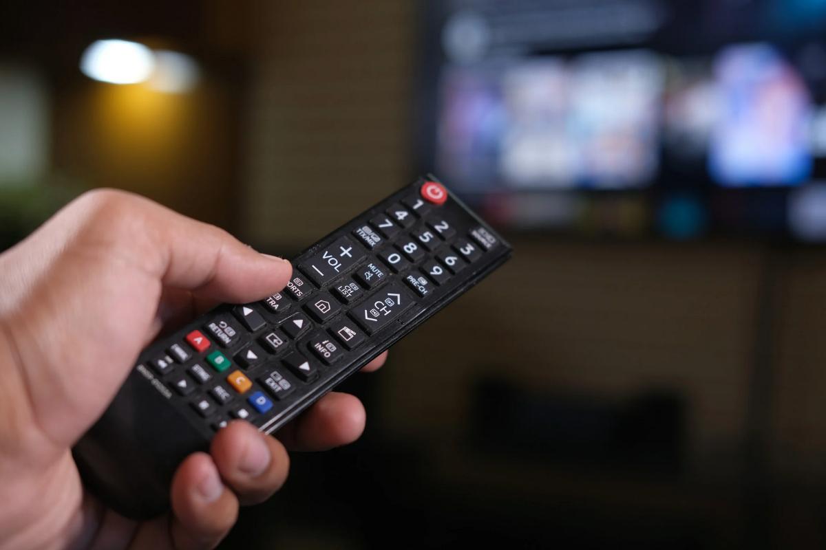 Mano che punta il telecomando verso la TV accesa