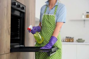 Donna con forno aperto e prodotto spray in mano