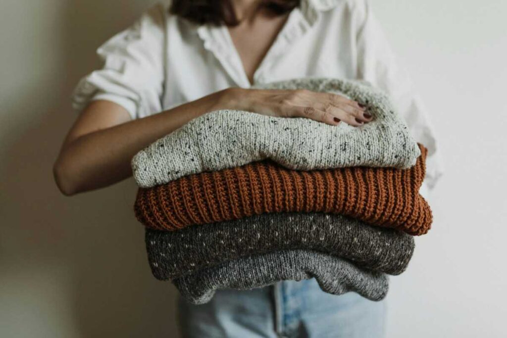 Donna che tiene pila di maglioni in mano